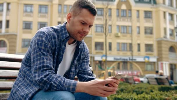 Profiili onnellinen kaveri käyttää älypuhelinta istuu penkillä puistossa
 - Materiaali, video
