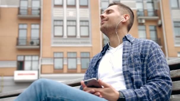 Крупный план молодого человека, сидящего на улице и слушающего музыку
. - Кадры, видео
