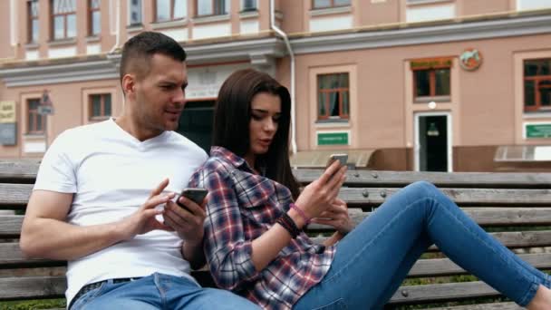 美しい若い女性の携帯電話を使用して、公園のベンチに座っている若い男に話して - 映像、動画