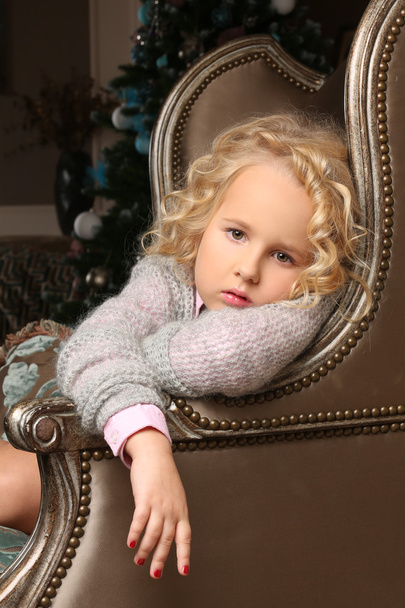 Cute little blond girl sitting peering over chair arms - Foto, Imagen