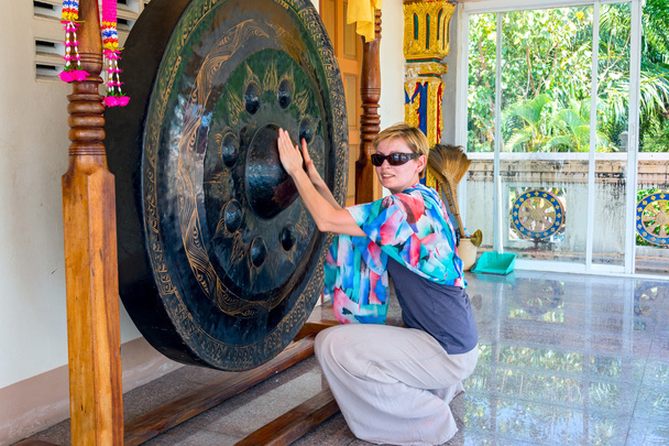 Big gong in a buddist temple, where you could see how clean is your karma. It is sayd that if a person has a pure karma - the gong will emit a loud buzz. Tourist woman checking her karma. - Photo, Image