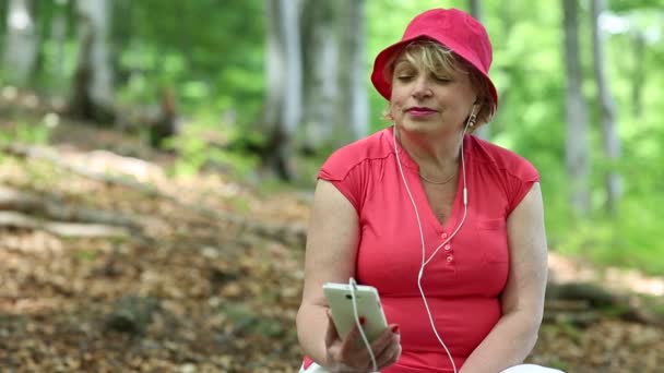 Frau in rotem T-Shirt und roter Mütze im Wald hört Musik - Filmmaterial, Video