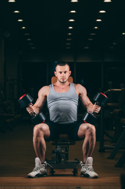 sport, bodybuilding, weightlifting, lifestyle and people concept - young man with dumbbells flexing muscles in gym - 写真・画像