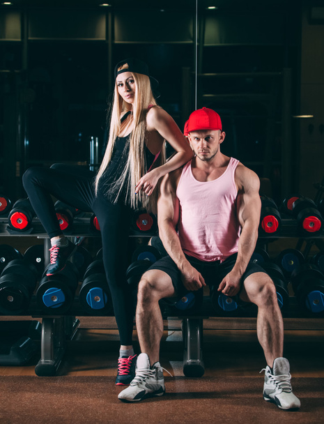 sport, bodybuilding, weightlifting, lifestyle and people concept - Young beautiful couple in stylish clothes sitting a gym near the dumbbells - Photo, image