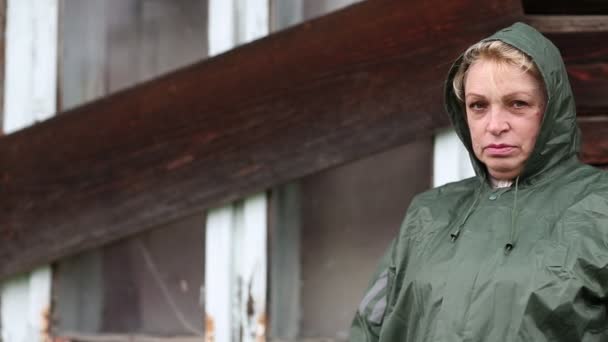 Γυναίκα σε πράσινο αδιάβροχο βρίσκεται κοντά στο ακατοίκητο σπίτι - Πλάνα, βίντεο