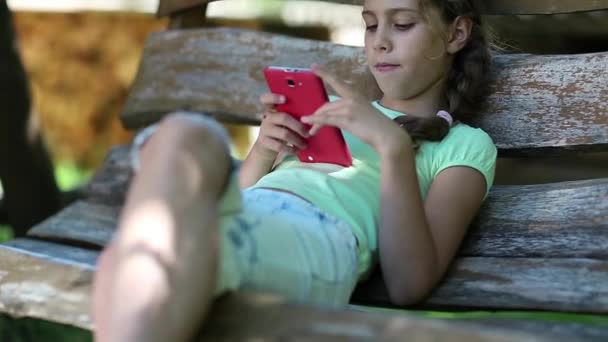 Mooi meisje met rode smartphone zit op de schommel-Bank - Video