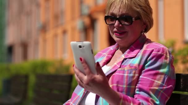 Frau sitzt auf Bank und kommuniziert per Smartphone - Filmmaterial, Video
