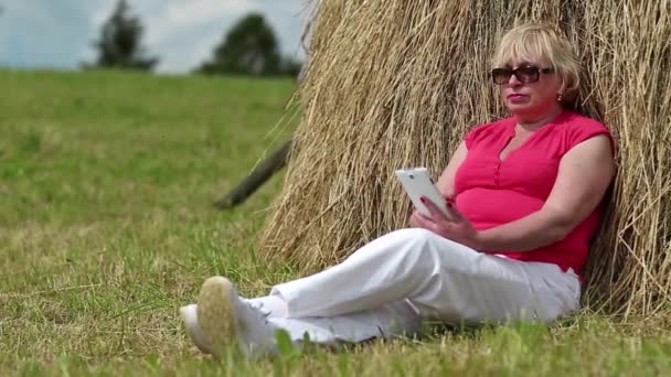 Женщина со смартфоном сидит возле стога сена
 - Кадры, видео