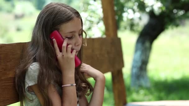 schönes Mädchen mit Smartphone sitzt auf der Bank im Garten - Filmmaterial, Video