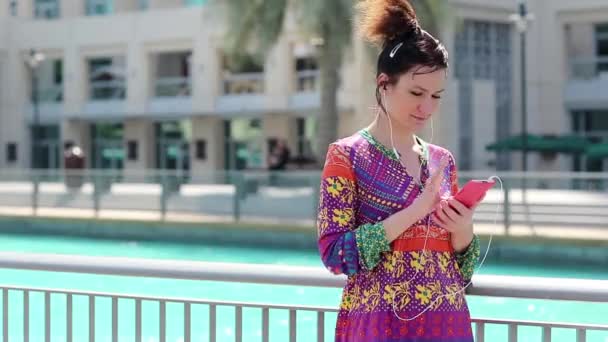 Žena s červeným smartphone a sluchátka poslouchá hudbu - Záběry, video