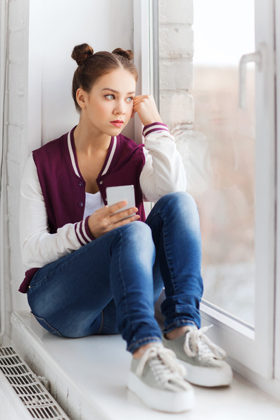 teenage girl sitting on windowsill with smartphone - Foto, afbeelding