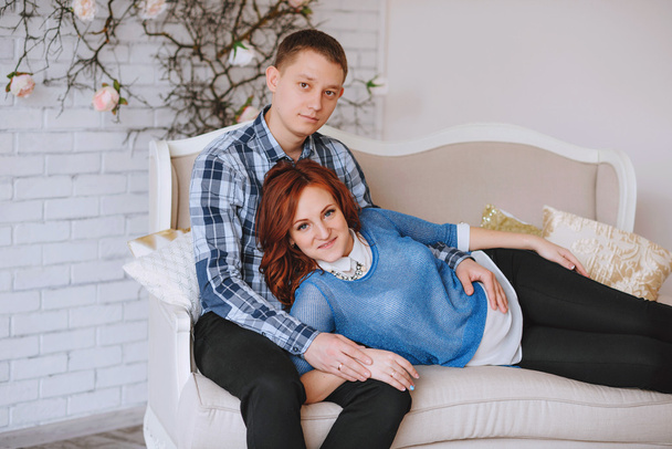 pregnant young couple in love couch. woman lay on knees of men. husband embraces his wife. With colors rose quartz and sky blue. - Photo, Image