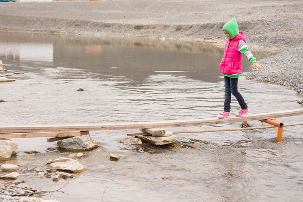 Маленькая девочка осторожно идет на доску через пруд
 - Фото, изображение