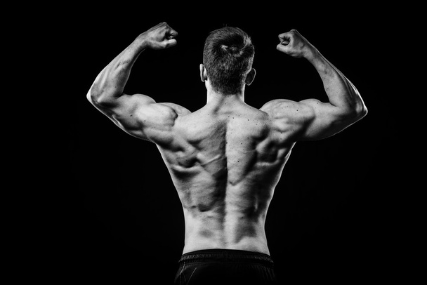 Sportowiec kulturysta młody i sprawny pokazuje widok na białym tle na czarnym tle z tyłu biceps - Zdjęcie, obraz