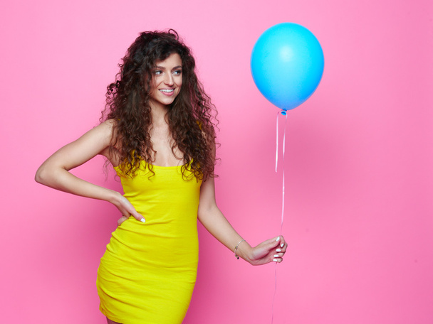Młoda i piękna dziewczyna kręcone w żółtej sukience na różowym tle niebieski balon i śmiech - Zdjęcie, obraz