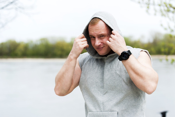 Workout man in hood resting by the river outdoor. - Photo, image
