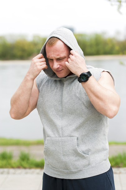 Workout man in hood resting by the river outdoor. - Photo, Image