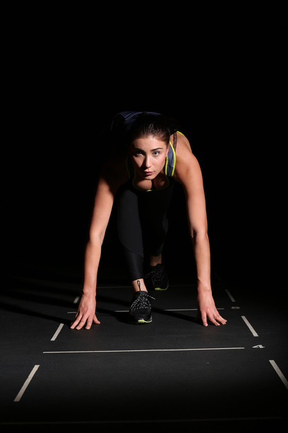Athletic woman in position ready to run on black background. - Zdjęcie, obraz