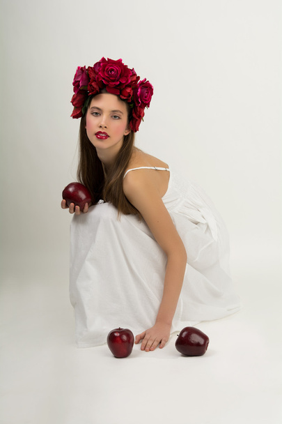 young beautiful girl in a white summer dress with a wreath of flowers on her head and apples on white background - Foto, immagini