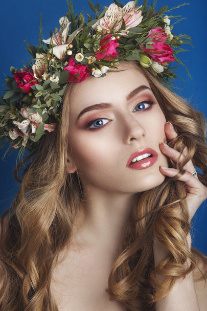 Beautiful young girl with a floral ornament in her hair on a blue background. Woman in wreath of flowers.Beauty Face. Fashion photo.Perfect makeup. Skin care concept. - Foto, Imagem