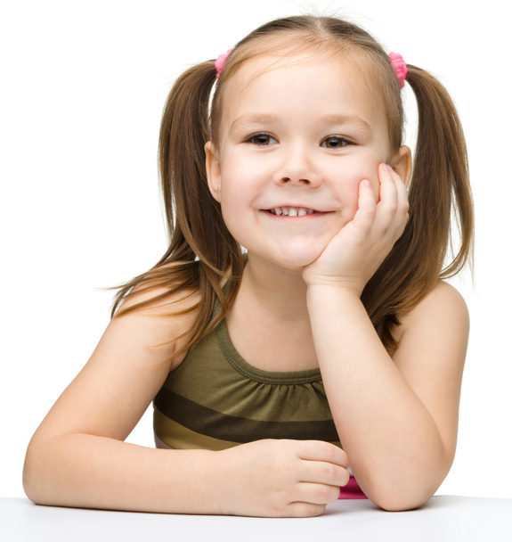 Onnellinen pieni tyttö istuu pöydässä ja hymyilee
 - Valokuva, kuva