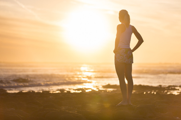 Nő a homokos strandon figyeli a naplemente. - Fotó, kép