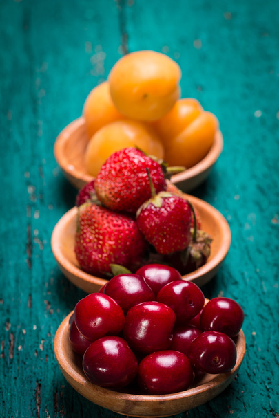 Fresh cherries,strawberries and apricots in a bowl on wooden green table. - Photo, image