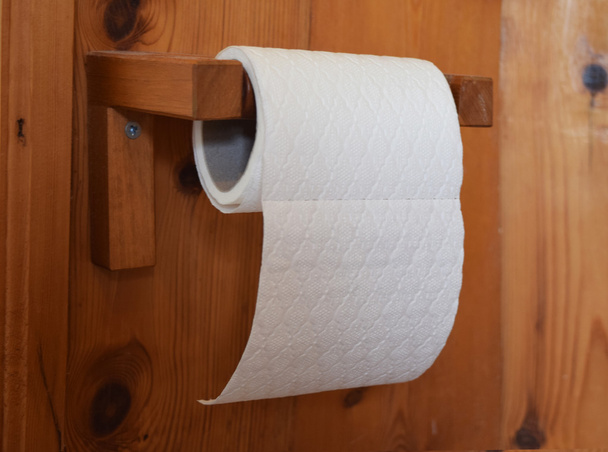 Roll of white patterned toilet paper hanging on wooden holder in a bathroom - Photo, Image