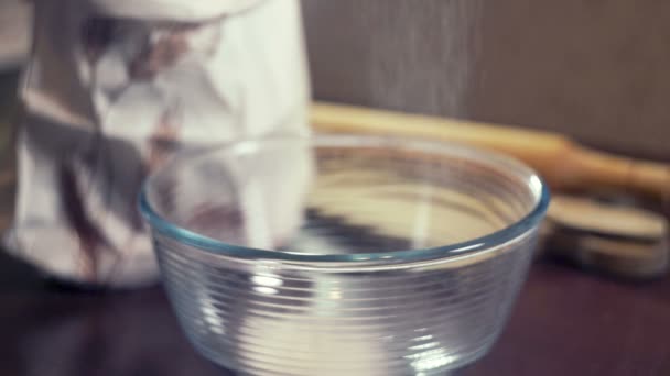 Σεφ κοσκίνισμα άχνη ζάχαρη για το γλάσο σε ένα βαθύ γυάλινο μπολ. Γλυκό καρύκευμα - Πλάνα, βίντεο
