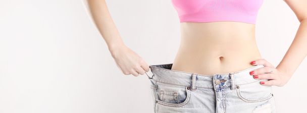 Студийный снимок молодой белой девушки, одетой в большие джинсы после диеты
 - Фото, изображение