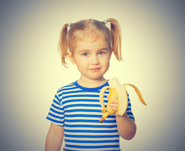 Pequeña chica divertida come plátano
. - Foto, Imagen