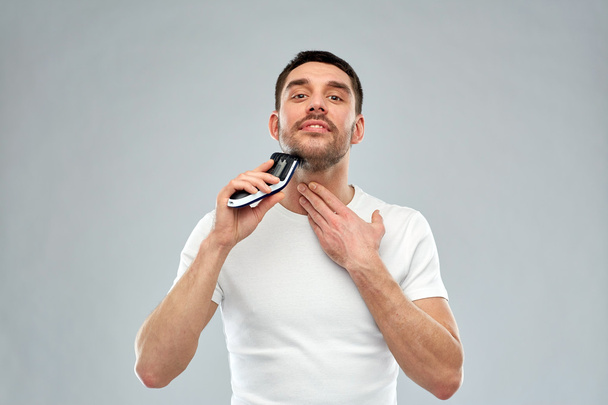 smiling man shaving beard with trimmer over gray - Fotografie, Obrázek