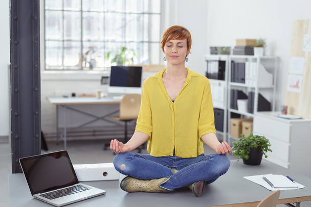 Woman sitting on desk in meditative pose - Foto, Imagem