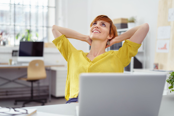 Carefree woman leaning back in office - Фото, изображение