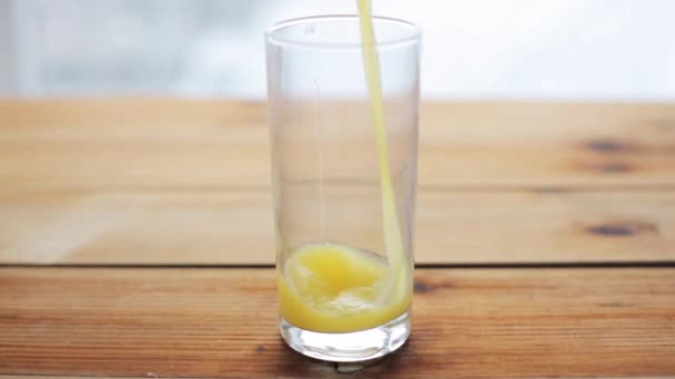 orange juice pouring into glass on wooden table - Filmati, video