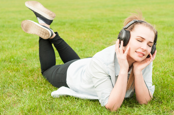 Young woman lying on grass and listen to music - Fotoğraf, Görsel