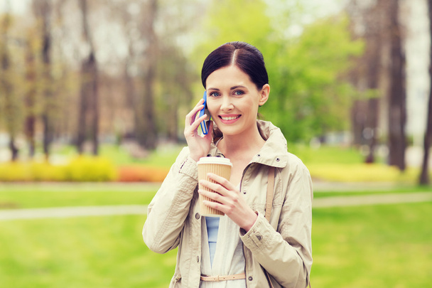 usmívající se žena s smartphone a kávy v parku - Fotografie, Obrázek