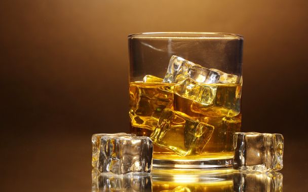 Glass of whiskey and ice on brown background - Photo, image