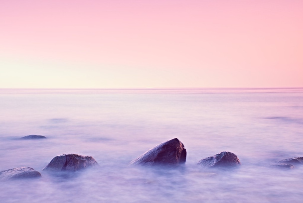 Romantic morning at sea. Big boulders sticking out from smooth water level. Pink horozon with first hot sun rays. - Photo, Image