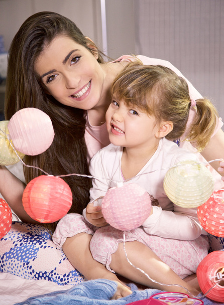 Happy mother and daughter in bed playing with cute pink lights looking camera smiling - Фото, зображення