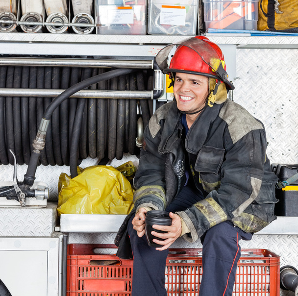Happy Fireman Holding Coffee Mug In Truck At Fire Station - Photo, image