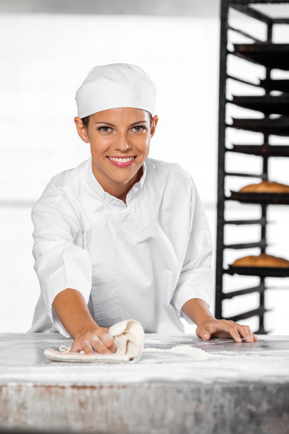 Confident Female Baker Cleaning Flour From Table - Foto, Imagen