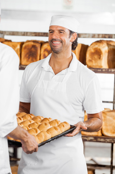 Baker Looking At Colleague While Carrying Bread Loaves - Φωτογραφία, εικόνα