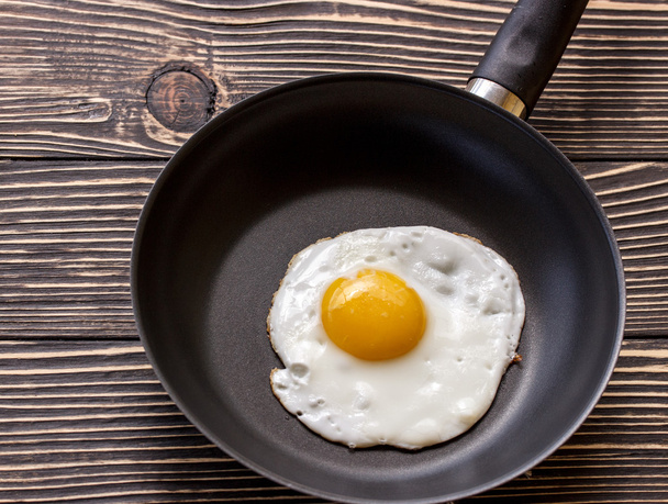 Fried sunny side up eggs on a pan on a brown oak old wooden board - Photo, Image