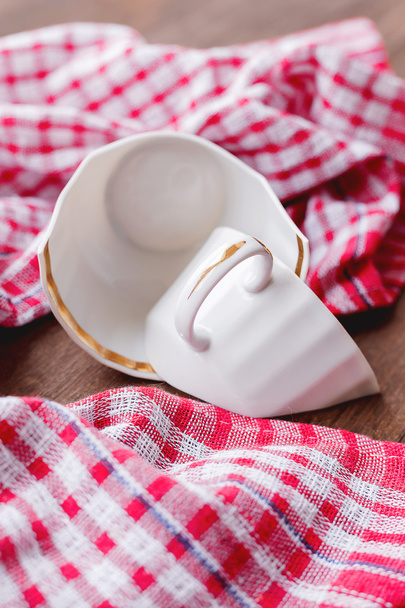 Broken white cup on wooden background with plaid red towel.  - Φωτογραφία, εικόνα