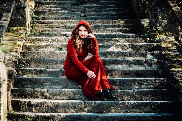 Mooie vrouw in rode jurk zittend op oude stappen - Foto, afbeelding