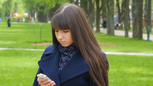 Krásná žena využívá mobilní smartphone venku v parku - detail. Mladá atraktivní šťastná dívka relaxuje v městském parku - Záběry, video