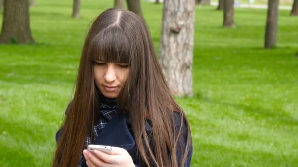 Mooie vrouw gebruikt mobiele smartphone buiten in het park - detail. Jonge aantrekkelijke gelukkig meisje ontspant in een stadspark en maakt gebruik van een mobiele telefoon. Ze ziet er erg blij en tevreden - Video
