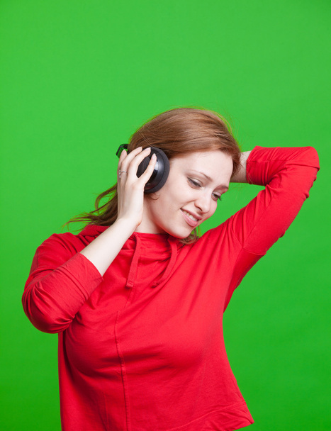Woman listening music on headphones on green background - Fotó, kép
