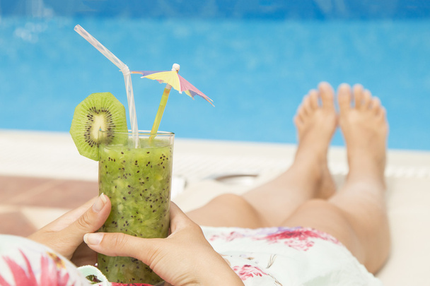 Female lying on sunbed and holding a glass of fresh kiwi smoothie  - Photo, Image